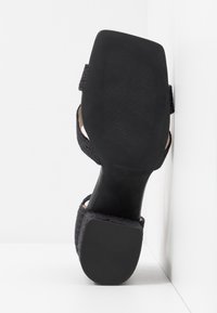 Sandale noire pour femme avec un bout carré et une semelle texturée, vue de dessous sur un fond blanc.