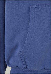 Blå bomulds hoodie med en lomme detalje, ribbet kant og blød tekstur. Stoffet fremstår glat med en let børstet finish.