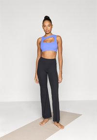 Μπλε αθλητικό crop top με λεπτομέρεια κοψίματος, συνοδευόμενο από μαύρο ψηλόμεσο παντελόνι με φαρδιά γραμμή. Λείο, ελαστικό ύφασμα και εφαρμοστή σχεδίαση.