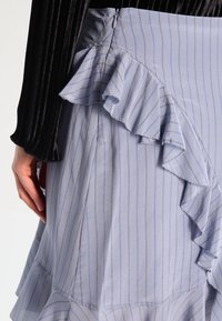 Ljust blå kjol med vertikala ränder och en fransad fåll, med en dold sidodragkedja och mjuk, flödande tygstruktur.