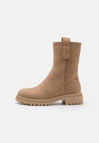 Bottine en cuir tan avec une texture lisse, bout rond, semelle plate en caoutchouc et une boucle à l'arrière pour un enfilage facile. Présente des détails de couture minimaux.