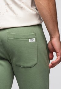 Groene sweatpants van een geweven stof, met een achterzak en een klein label. De tailleband is elastisch en sluit goed aan.