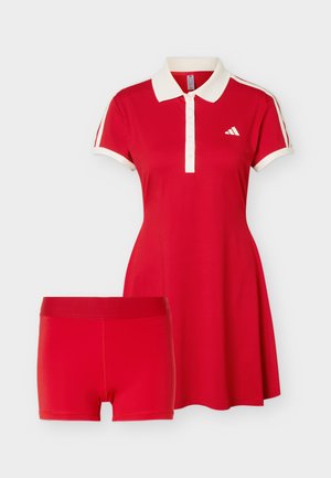 Robe de tennis rouge à manches courtes avec col blanc et rayures sur les manches, associée à un short rouge assorti.