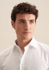 Biała koszula z rozkładanym kołnierzykiem, zapięciem na guziki i kontrastowym wzorem wyko�ńczenia wewnątrz kołnierzyka. Gładka faktura tkaniny.