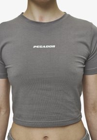 Sivo skrajšano majico iz lahkega materiala, z okroglim izrezom in belim logotipom "PEGADOR" na predelu prsi.