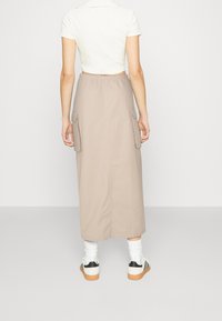 Jupe cargo beige avec poches latérales, coupe droite, taille élastique, et tissu doux en mélange de coton ; portée avec des chaussettes blanches et des baskets.