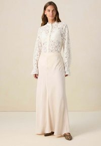 Kanten blouse met lange mouwen en hoge hals, gecombineerd met een vloeiende lichtroze rok. De outfit heeft subtiele details en een natuurlijke textuur.