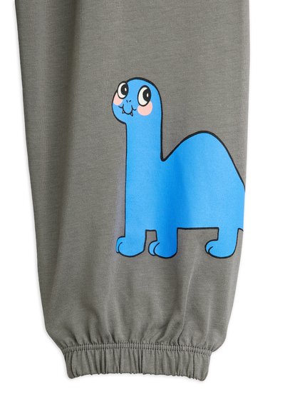 Šedé tepláky s modrou grafikou dinosaura s usmievavou tvárou. Pás má elastické zhrnutie. Hladká textúra látky.