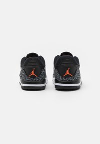 Black sneakers with a textured gray and black pattern on the heel, orange logo accents, and a white midsole. Breathable mesh upper.