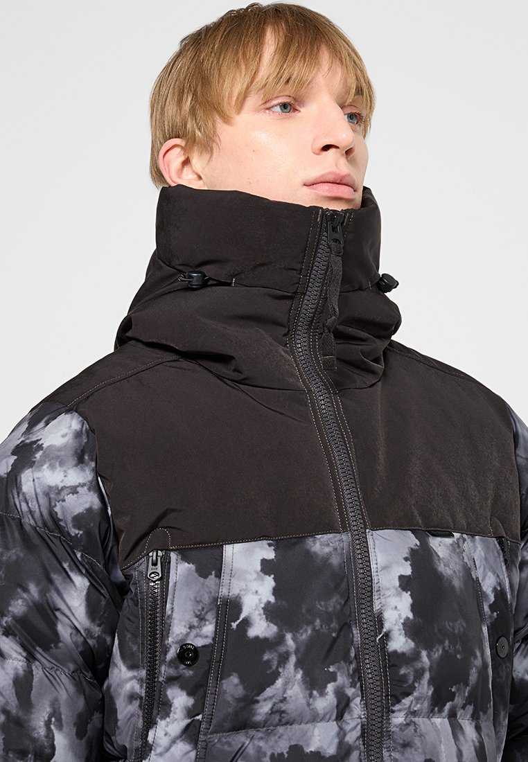 Puchowa kurtka z wysokim kołnierzem. Górna część w jednolitym czarnym kolorze; dolna w szarym i czarnym wzorze w chmurki. Posiada zamek błyskawiczny i zapięcia na guziki.