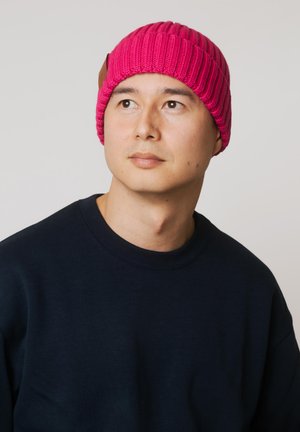 Różowa dziergana czapka z prążkowaną fakturą i skórzaną ozdobą. Noszona z granatowym swetrem typu crewneck, z okrągłym dekoltem i luźnym krojem.