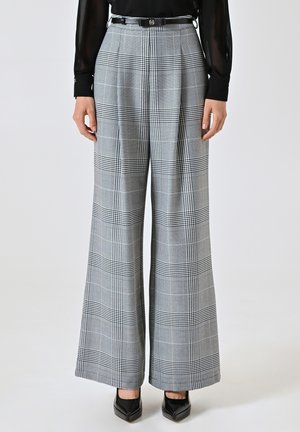 Weite Hosen im grau-schwarzen karierten Muster. Mit Falten, einer taillierten Taille mit einem Gürtel und eleganten schwarzen Schuhen. Strukturierter Stoff.