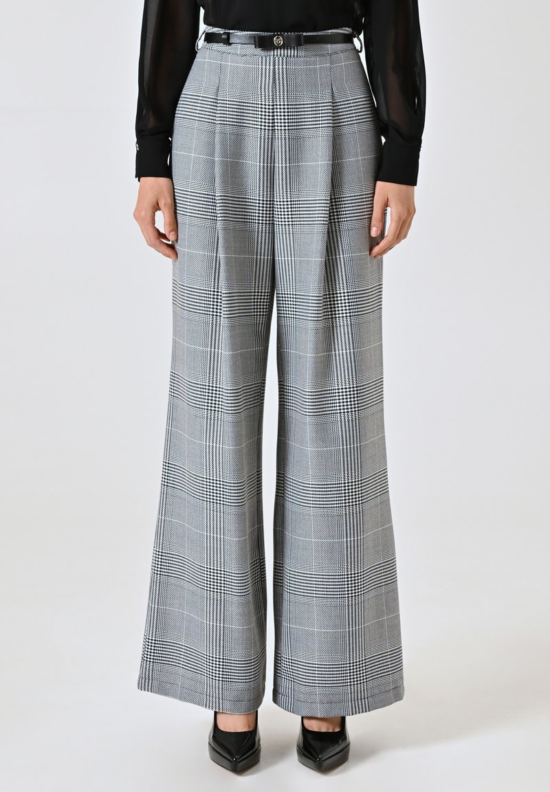 Wijdvallende broek in een grijs-zwart ruitpatroon. Bevat plooien, een strakke taille met een riem en stijlvolle zwarte schoenen. Getextureerd materiaal.