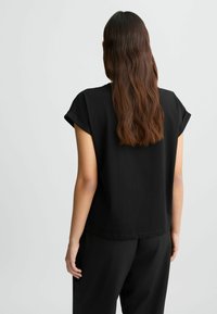 Top corto nero a maniche corte realizzato in tessuto morbido, caratterizzato da una vestibilità ampia e scollatura tonda. Design semplice senza motivi o accessori visibili.