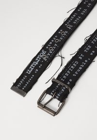 Zwarte stoffen riem met gedrukte tekst, zilveren metalen gesp en oogjes; heeft franjeranden en een gestructureerd oppervlak.