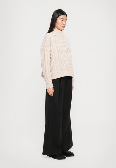 Light beige cable-knit sweater with a high collar, paired with loose black trousers. The outfit features a relaxed silhouette and textured fabric.