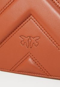 Oranžinė dirbtinė oda su deimanto formos siuvinėjimu. Turtingos reljefinės logotipo ir kontrastingos siūlės. Lygi tekstūra su nedideliu blizgesiu.