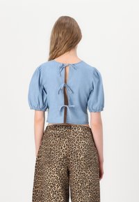 Ljusblå denimcropptröja med puffärmar och ett ryggutskärning som är fastsatt med tre knutna rosetter. I kombination med leopardmönstrade vida byxor.
