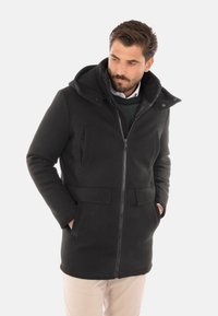 Cappotto neri con zip e cappuccio, dotato di due tasche frontali e tessuto testurizzato. Il design include un colletto rialzato e una fodera morbida.