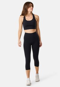 Reggiseno sportivo nero e leggings capri a vita alta realizzati in tessuto elastico, caratterizzati da un design aderente e una texture liscia.