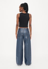 Cropped black tank top with wide-leg blue denim jeans. Jeans feature back pockets, visible stitching, and a shiny texture.