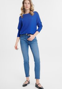 Maglione lavorato a maglia di un blu royal, colletto rotondo e maniche lunghe abbinato a jeans chiari a vita alta. Modella con ballerine nere per creare un contrasto.