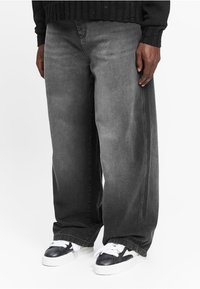 Wide-leg jeans in a gradient dark gray wash, featuring a classic denim texture and contrasting stitching, paired with black and white sneakers.