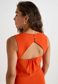 Vestido naranja sin mangas con un escote en forma de llave en la parte posterior y detalles fruncidos, adornado con tres botones decorativos. Textura suave.