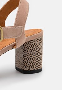 Beige Wildledersandalette mit einer strukturierten orangen Innensohle und einem gemusterten Absatz in Hellbraun und schwarzen Akzenten. Sechseckiges Basisdesign.