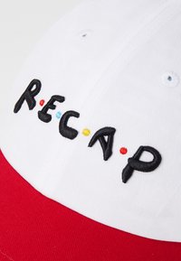 Casquette blanche et rouge au design structuré. Présente un texte brodé "R.E.C.A.P" en accents noirs, bleus, jaunes et rouges. Tissu texturé.