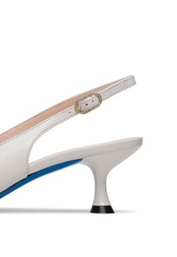 Sandal in pelle bianca con tacco curvo basso, dettaglio blu e una fibbia dorata adornata di strass. Texture liscia, design moderno.