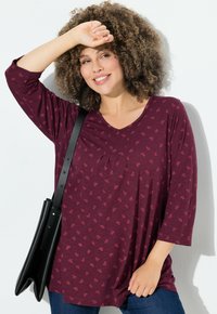 Top lungo color marrone scuro con scollo a V, caratterizzato da un motivo sottile. Abbinato a jeans blu e una borsa a spalla nera. Tessuto dalla texture liscia.