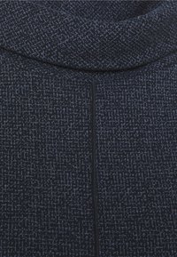 Gros plan sur un tissu sombre plié avec un motif fin tacheté gris clair et une couture centrale verticale.