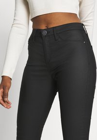 Jeans de tiro alto negros con una textura suave, que presentan un cierre de botón en el frente, costuras sutiles y un diseño ajustado.