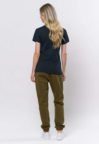 Črna majica s kratkimi rokavi v kombinaciji z ohlapnimi olivno zelenimi hlačami z ožanimi hlačnicami. Hlače imajo elastične manšete in so stilirane z belimi supergami.