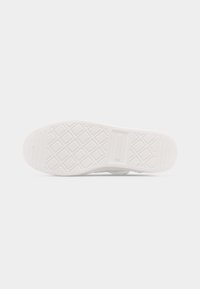 Semelle d'une chaussure en caoutchouc blanche avec un motif de crampons en formes de losanges et de lignes, et un panneau rectangulaire pour le logo au centre.