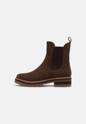 Bottine en cuir marron avec panneau latéral élastique, languette de traction et semelle à crampons avec petit talon empilé sur fond blanc.