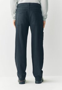 Black denim cargo pants with a relaxed fit, featuring two back pockets and a side pocket, finished with stitching details and a flat waistband.