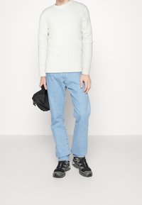 Biały sweter z warkoczowym splotem, jasnoniebieskie dżinsy, czarny plecak oraz czarne buty sportowe z szarymi akcentami. Minimalistyczny design, luźny krój.