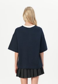 Námornícky oversize tričko s krátkymi rukávmi, okrúhlym bielym golierom a rovnými okrajmi, v kombinácii s čiernou plisovanou sukňou. Hladká textúra látky.