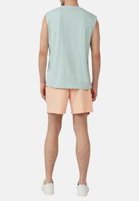 Helles blaues ärmelloses Shirt aus Baumwolle, kombiniert mit pfirsichfarbenen Shorts. Weiße Sneakers. Ansicht von hinten, mit Fokus auf die Farben und Formen der Kleidung.