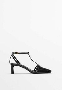 Chaussures à talon en cuir noir avec un bout pointu, une bride de cheville avec une boucle dorée et des panneaux latéraux transparents. Design à talon bloc modéré.