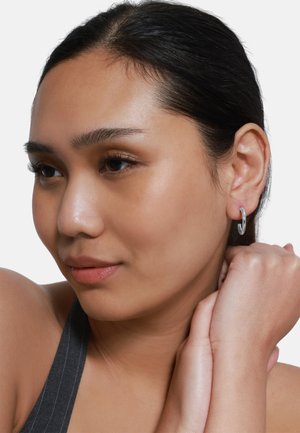 Boucle d'oreille en argent avec une finition lisse et polie, présentant un design ouvert, portée à l'oreille droite sur un fond clair.