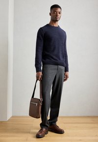 Navy knit sweater with crew neck, gray tailored trousers, brown leather shoes, and a small brown bag with a silver zipper.