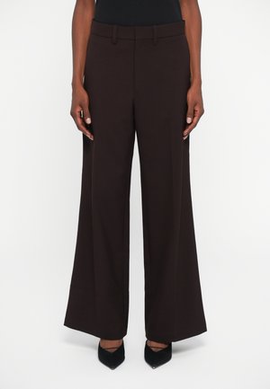 Bruine wijde broek gemaakt van een gladde stof. Heeft een aansluitende tailleband en zijzakken, gestyled met spitse zwarte hakken.