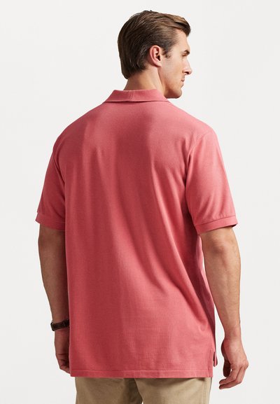 Πόλο μπλουζάκι σε κοραλί χρώμα, φτιαγμένο από υφασμένο ύφασμα. Διαθέτει γιακά, κοντά μανίκια και ελαφρώς καμπύλη αίσθηση στο τελείωμα με πλαϊνές σχισμές.