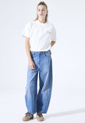 Wit katoenen T-shirt met de tekst "Breakfast Club" links op de borst. Brede blauwe spijkerbroek met grote pijpen, uitgevoerd in het klassieke vijfzakkenmodel.