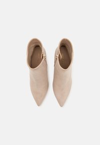 Bottines en daim beige avec un design à bout pointu et une fermeture éclair sur le côté, présentant une texture lisse et un style minimaliste.