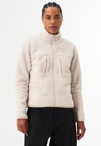 Fleece-Jacke mit Reißverschluss in Hellbeige, mit hohem Kragen, zwei Brusttaschen und glatter Textur. Akzente durch dezente Logos und kontrastierende Einfassungen.