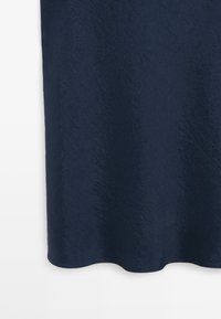 Dunkelblauer, zerknitterter Satinstoff mit leichtem Glanz und geschwungenem Saum vor weißem Hintergrund.